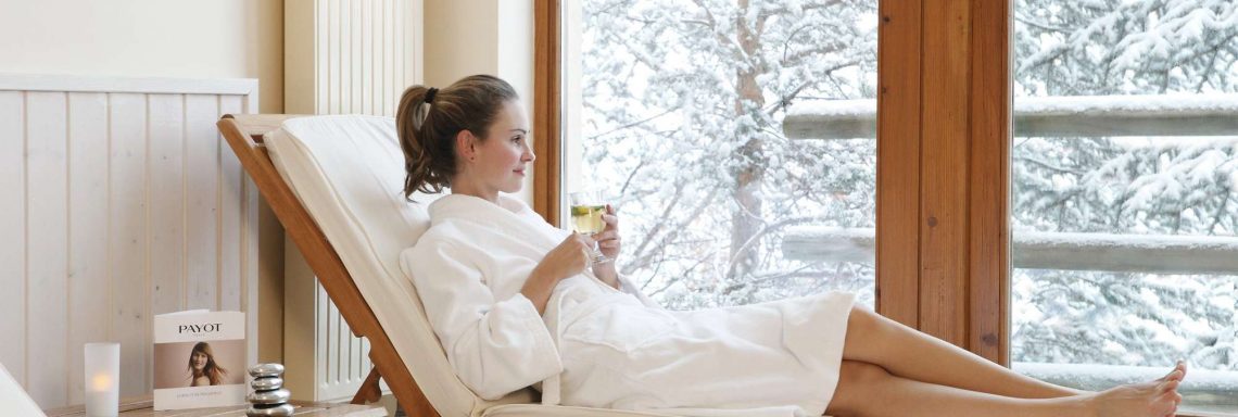 Club Med Serre-Chevalier, en France - Image d'une femme en peignoir allongée sur un transat en intérieur avec vue sur le paysage enneigé