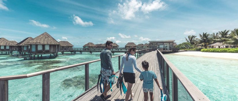 Club Med Kani, aux Maldives - Une famille marche sur un pont de bois, surplombant l'Océan. 