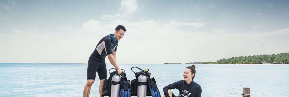 Club Med Villas de FInolhu, aux Maldives - Photo de deux personnes souriantes s'apprêtant à plonger devant l'océan avec bonbonnes