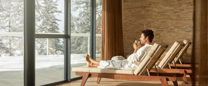 Club Med Arcs Panorama, en France - Un homme est allongé sur une chaise longue face à une large fenestration 